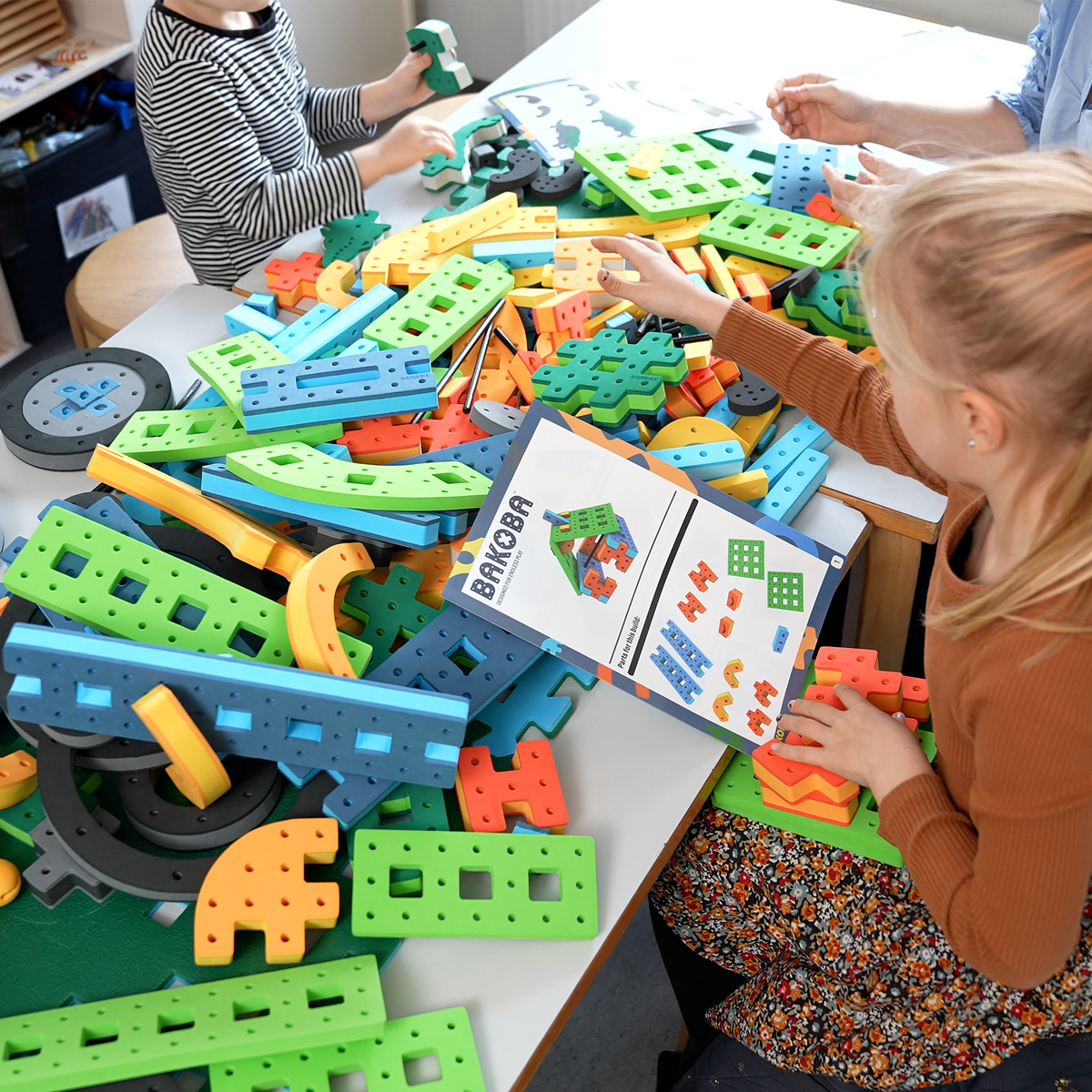 A young girl using an official BAKOBA instruction manual to assemble colorful foam construction toys