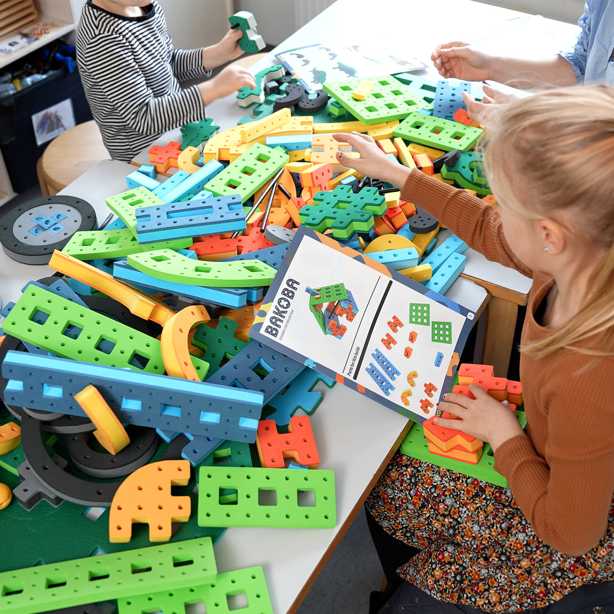 A young girl using an official BAKOBA instruction manual to assemble colorful foam construction toys.